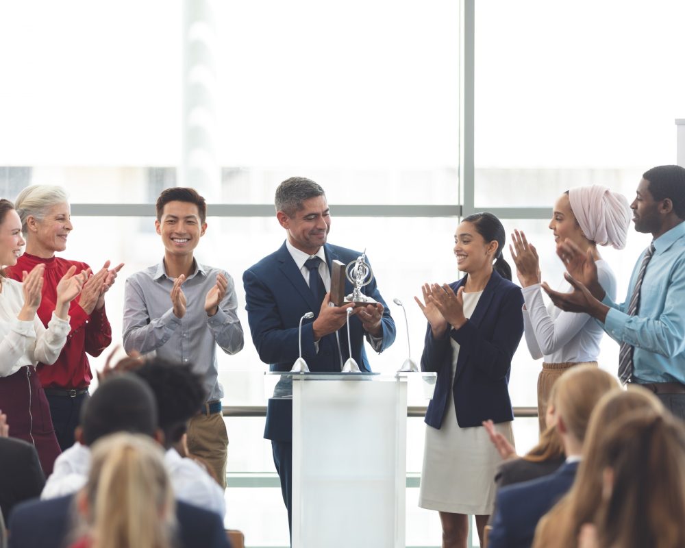 businessman-holding-award-on-podium-with-colleagues-at-business-seminar.jpg