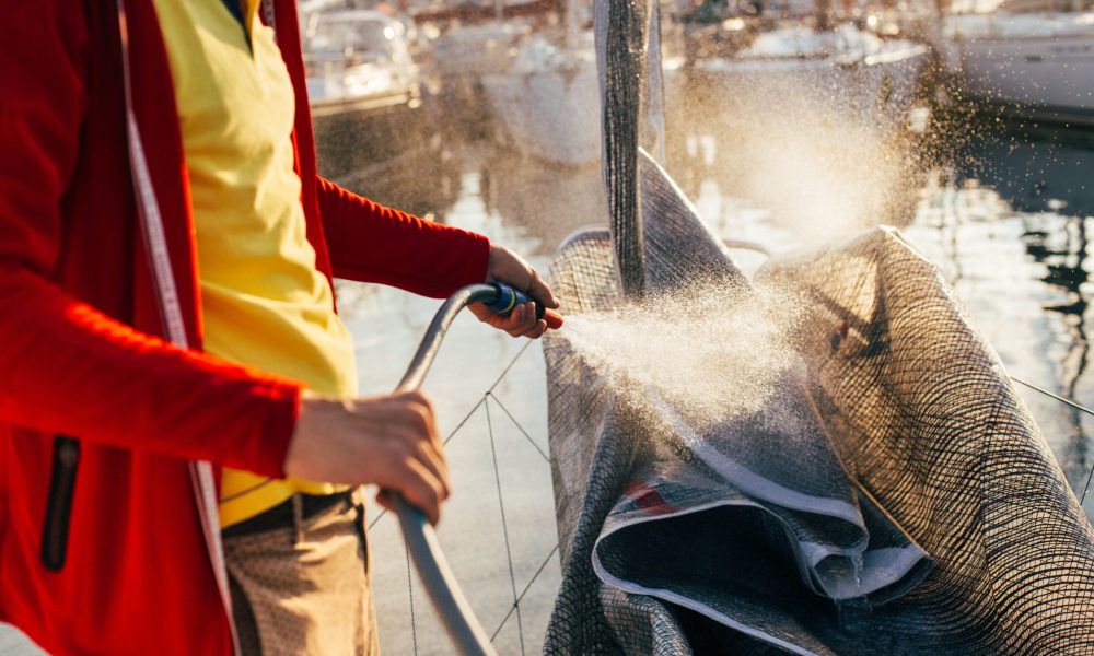 Soft focus of water drops come out of hose, sailor or captain, yacht owner washes salty residue from sail, mainsail or spinnaker, when sailboat is docked in yard or marina, after race or competition